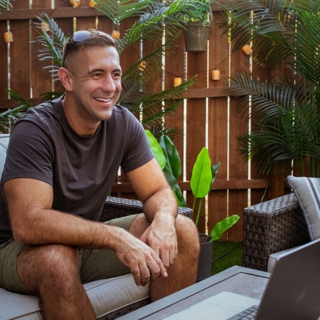 Ryan Tanel smiling, seated outdoors with a laptop